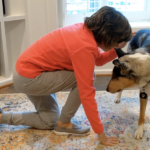 woman on the ground kneeling partially getting up next to a standing service dog